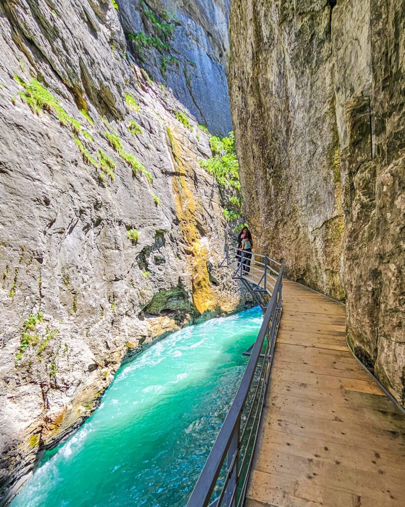 Wooden boardwalk along the cliff above the turquoise Aare, with an orange-streaked rock face