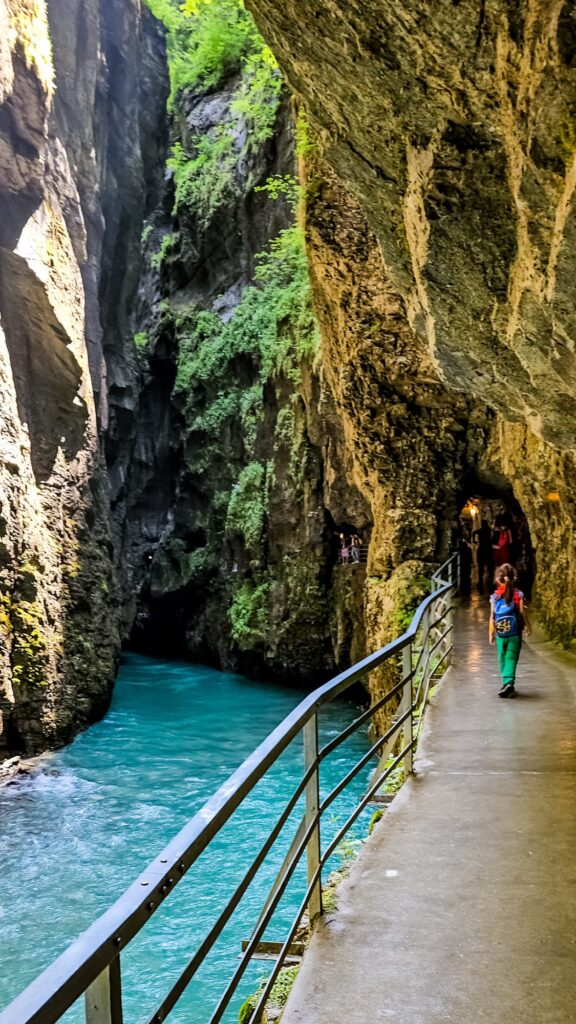 A child walking along the path towards a lit tunnel beside the turquoise Aare