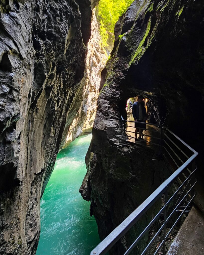 Dark, narrow slot of the Aare Gorge with a walkway and a lit tunnel above turquoise water