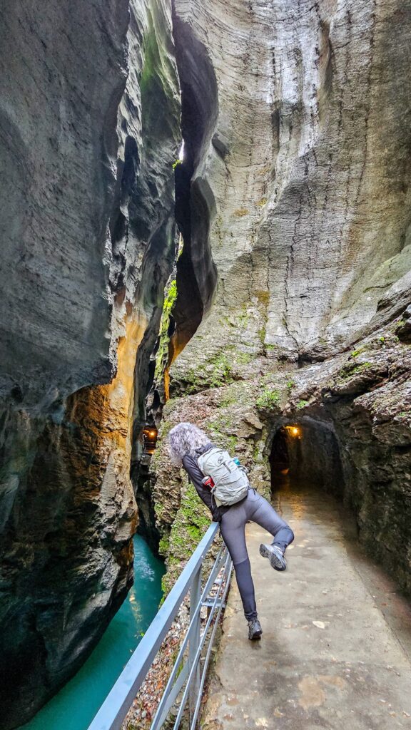 Woman jumping playfully on the path beside a lit tunnel in the narrowest part of the gorge