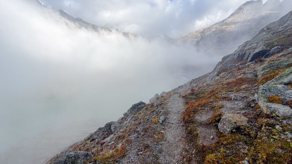 Path along a slope with rust-coloured grass, fog filling the valley below