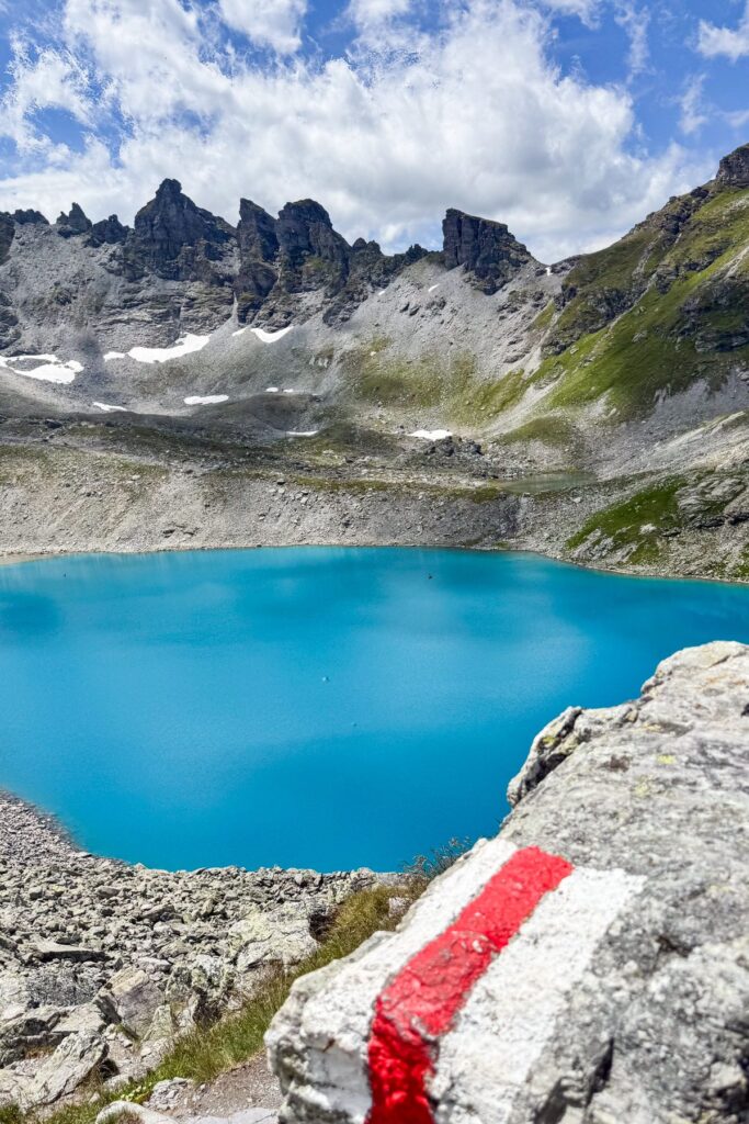 Turquoise Wildsee below jagged peaks, with a red and white trail marker on a rock