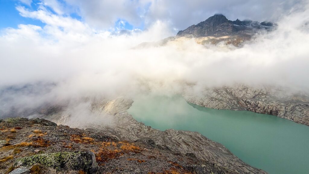 Fog lifting over the Rhône Glacier lake, with a rocky peak behind