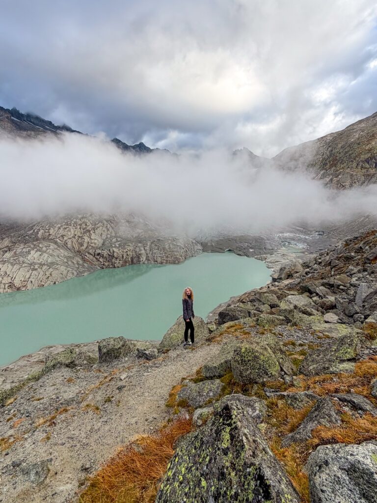 Walker looking back over the Rhône Glacier lake from a rocky slope in autumn